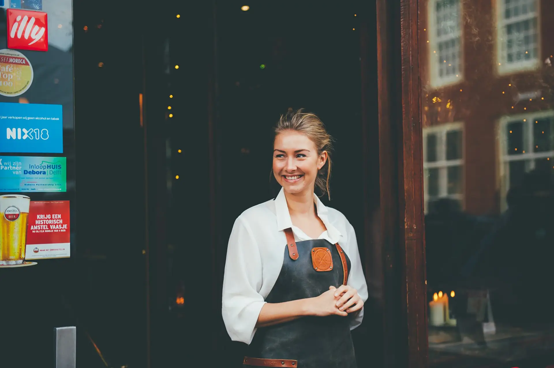 Lachende vrouwelijke ober die naar buiten komt lopen vanuit haar restaurant