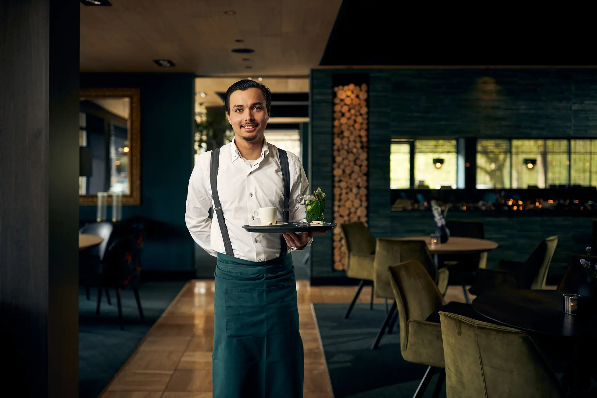 Lopende ober met een dienblad in een restaurant met groen/blauwe tinten