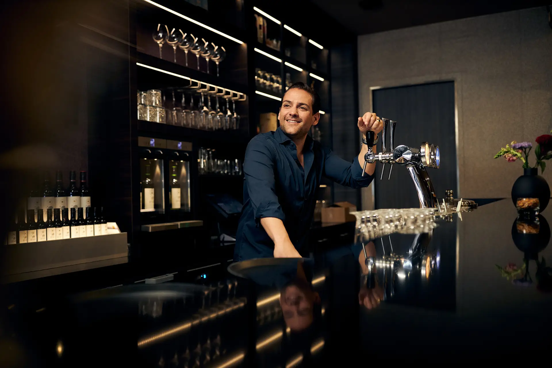 Man die achter de bar staat en met zijn hand rust op een biertap