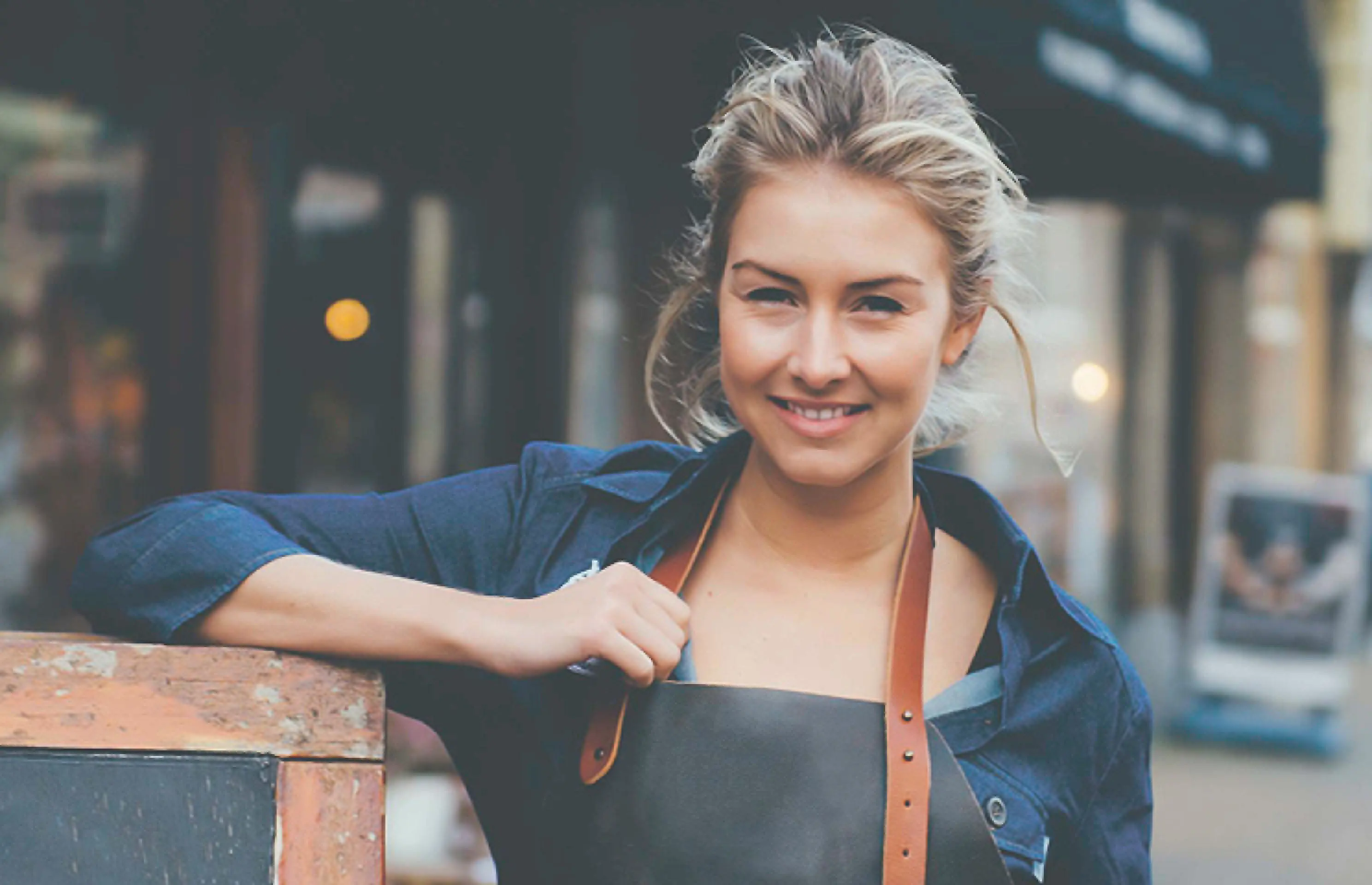 Medewerker bediening leunt op menubord en kijkt lachend in de camera