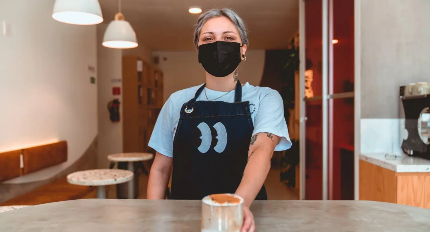 Medewerker bediening met mondkapje op, serveert kop koffie