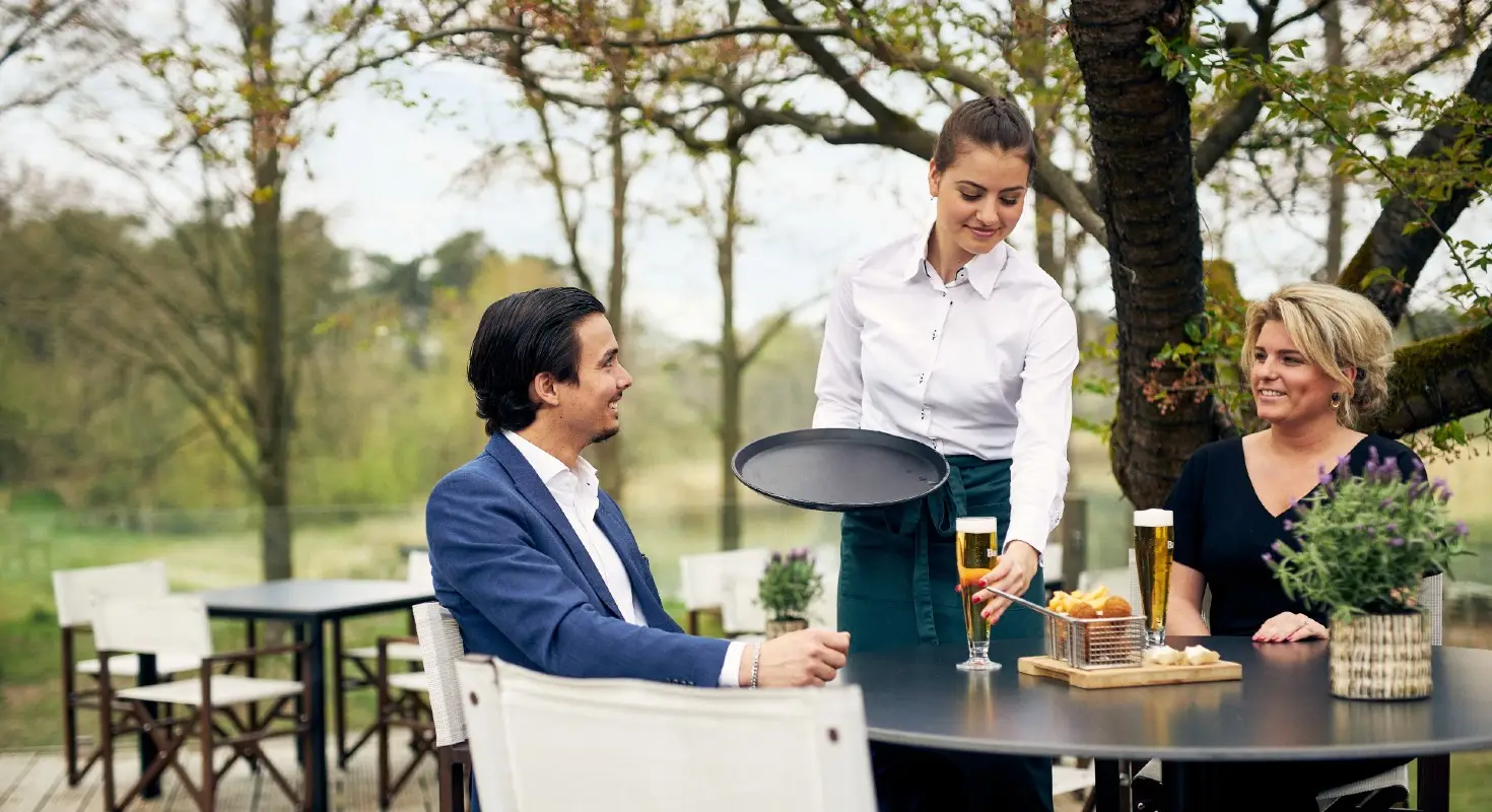 Medewerker bediening serveert bier aan gasten op terras