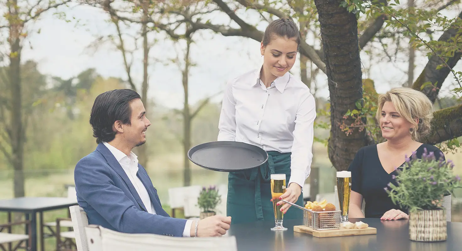 Medewerker bediening serveert bier aan gasten op terras