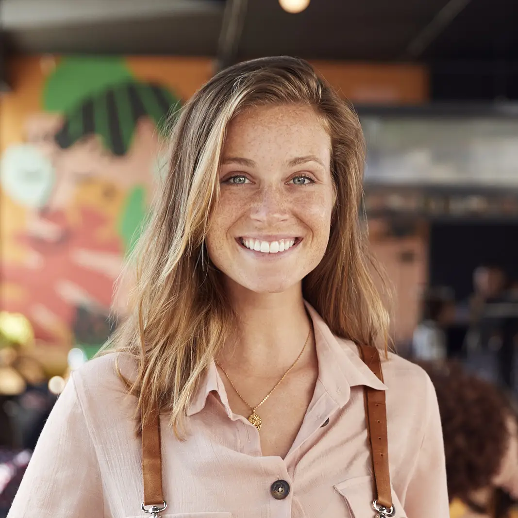 Medewerker bediening staat in café met gasten en kijkt lachend naar de camera