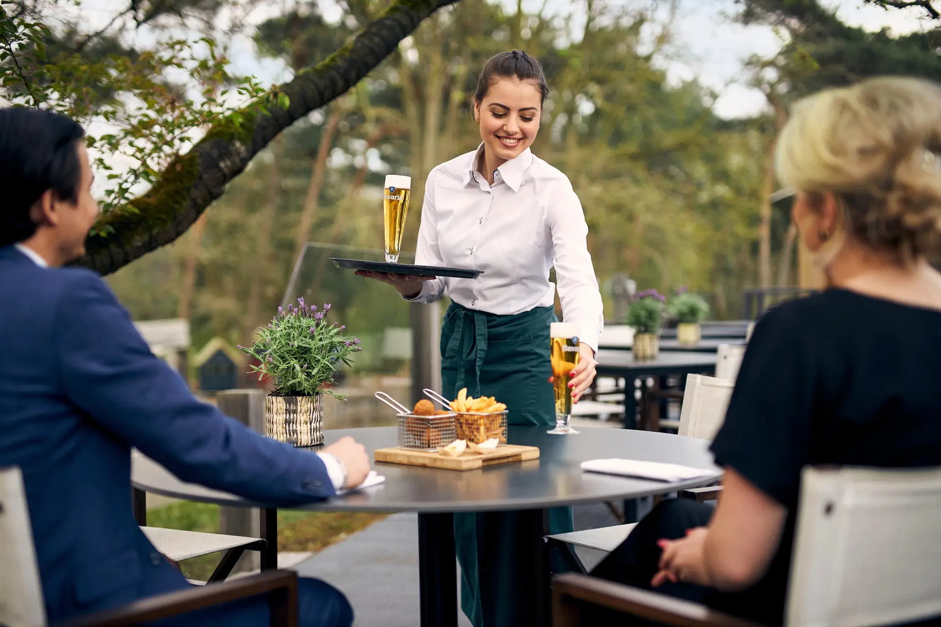 Serveerster zet een glas wijn neer buiten op een terras met een man en een vrouw