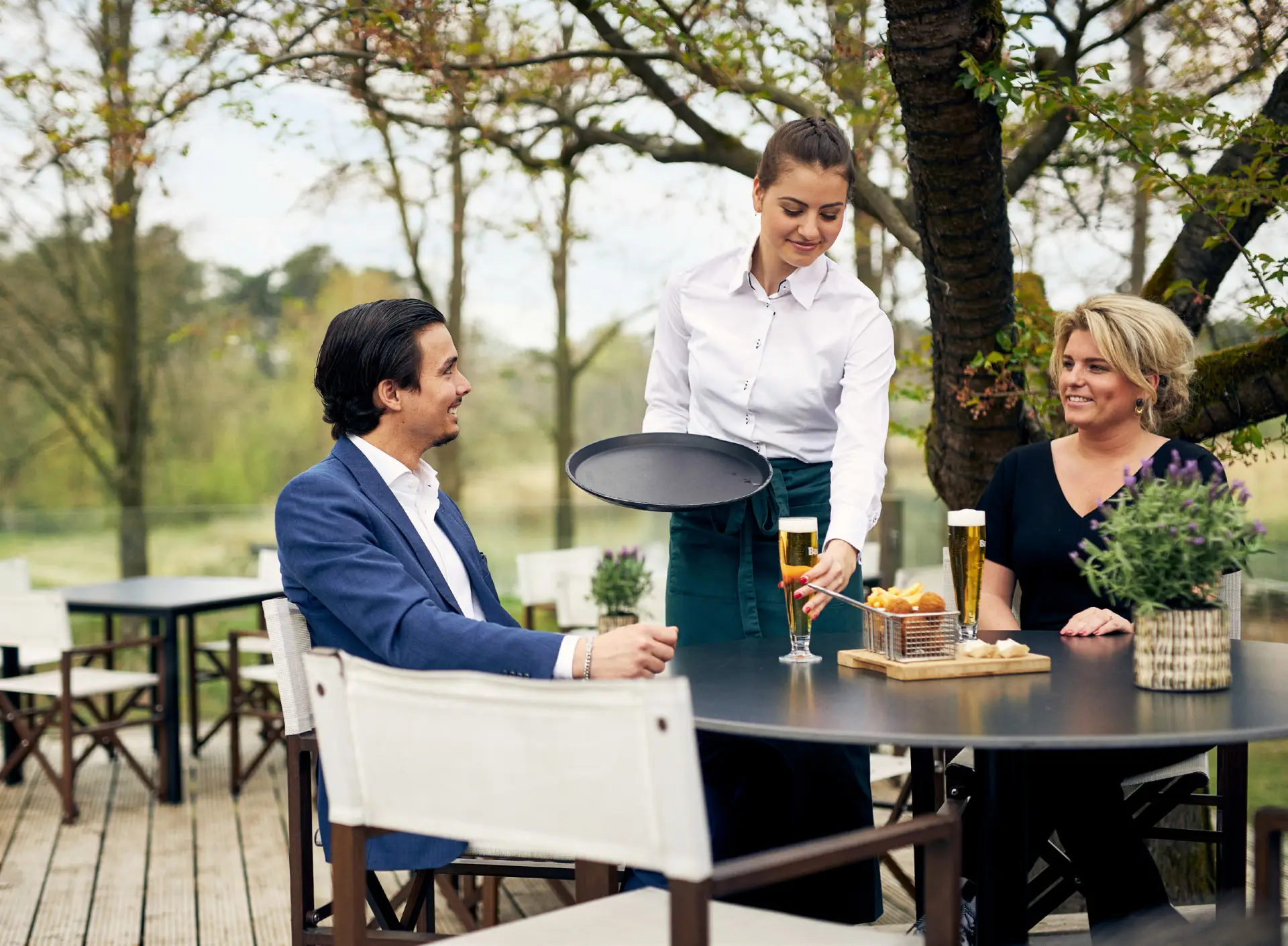 Serveerster zet een glas wijn neer buiten op een terras met een man en een vrouw