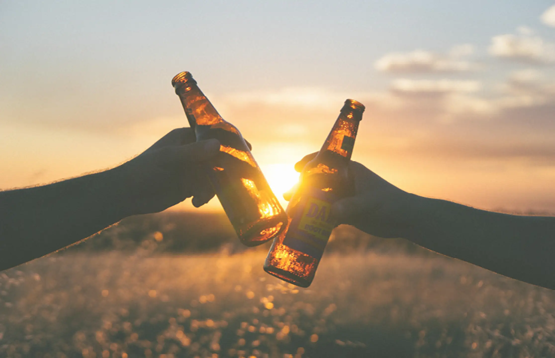 Twee mensen proosten met een biertje bij de ondergaande zon