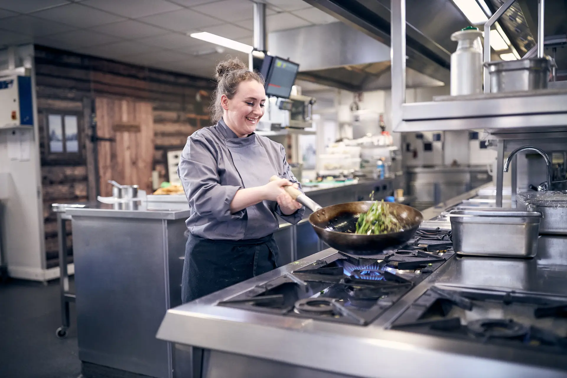 Vrouwelijke kok met een wok in een industriële keuken