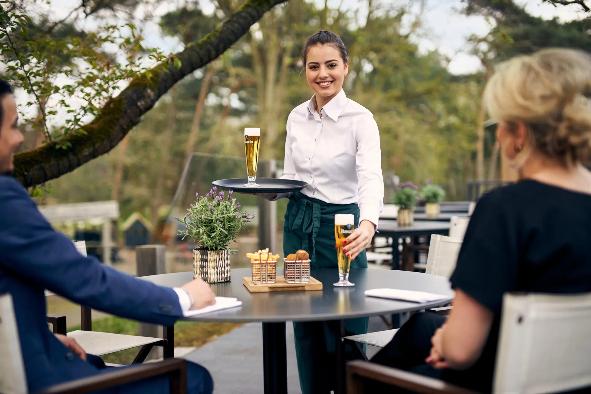 Vrouwelijke ober die een glas bier neerzet op tafel op het terras